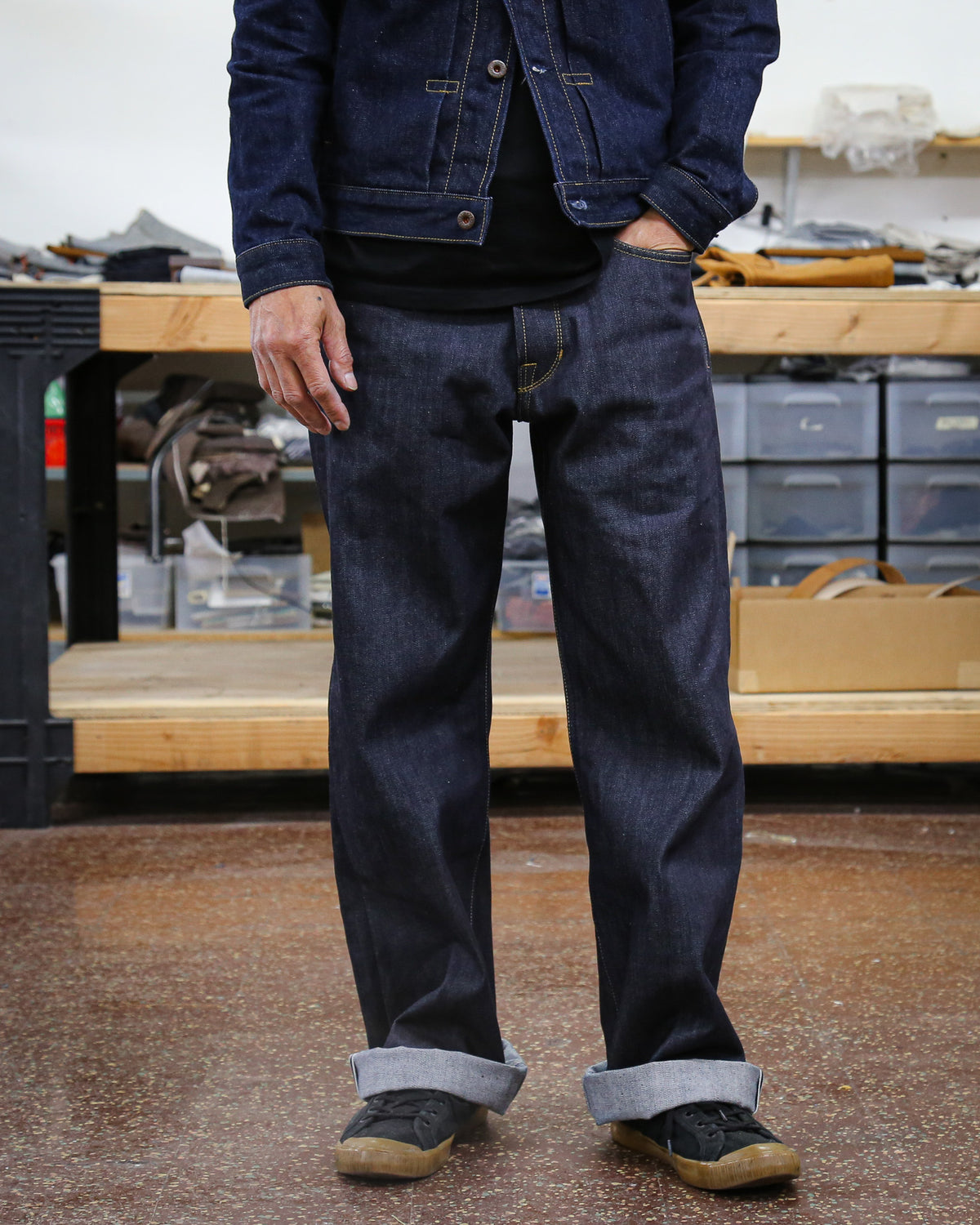Person wearing dark blue jeans and a denim jacket in a workshop setting.