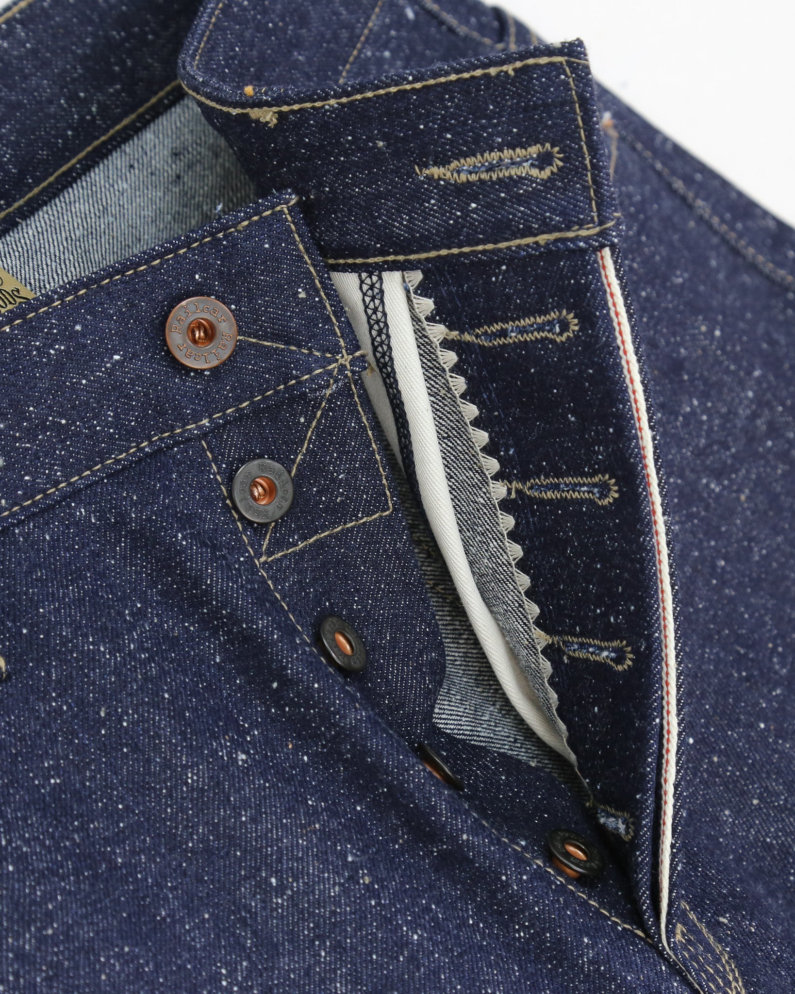 Close-up of blue denim fabric with stitching and buttons on a white background