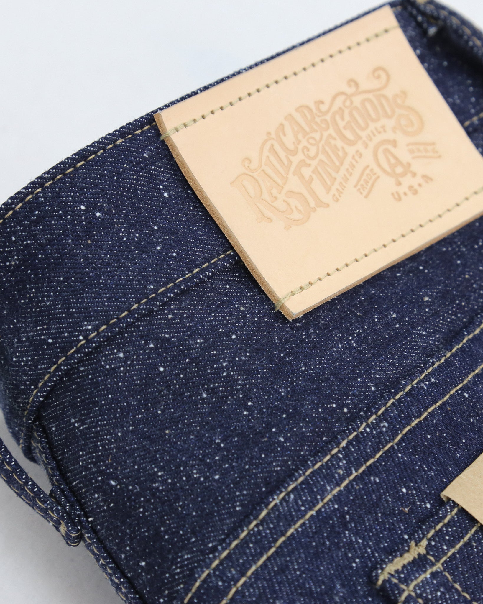 Close-up of blue denim fabric with a leather label on a light gray background